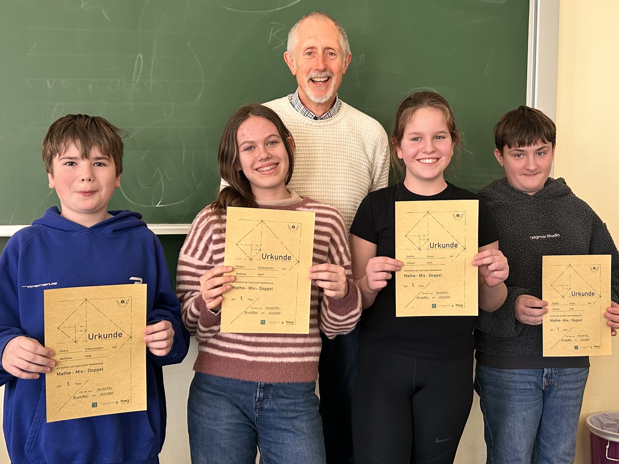 Mathelehrer steht mit SchülerInnen vor einer Schultafel 