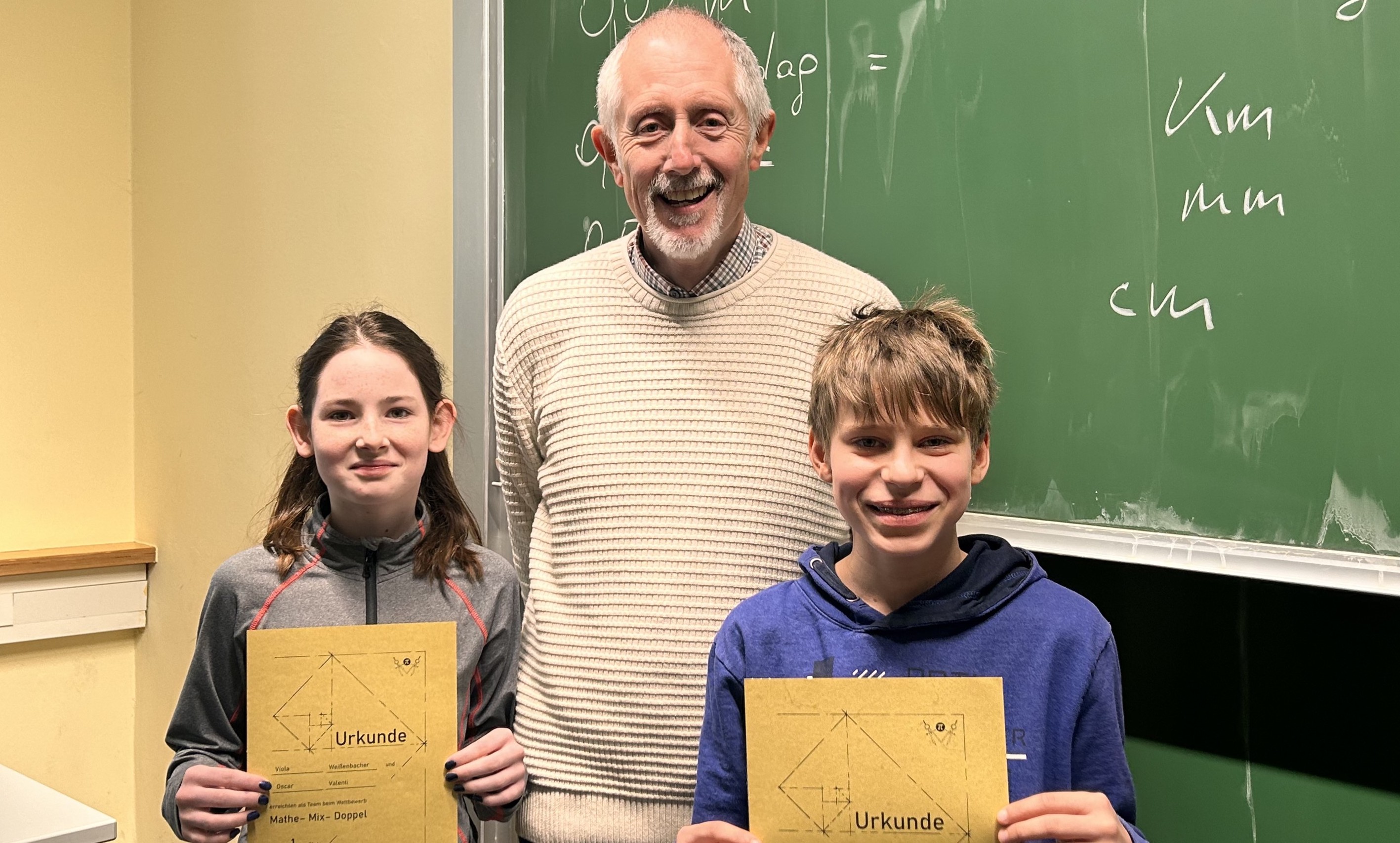 Mathelehrer steht mit SchülerInnen vor einer Schultafel 