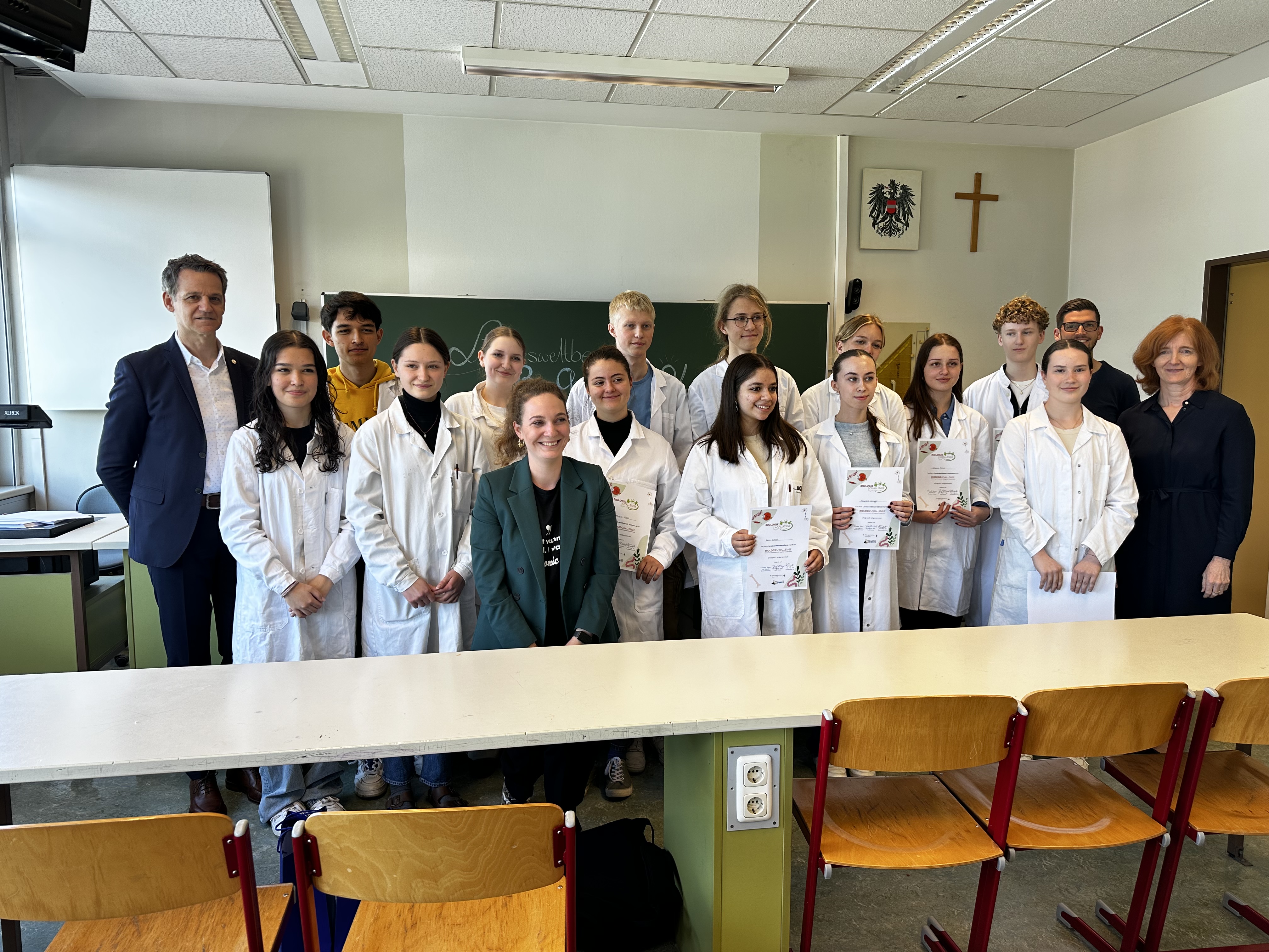 Eine Gruppe Schüler und Schülerinnen mit ihren Lehrerinnen in einem Klassenraum. Alle tragen weiße Laborkittel